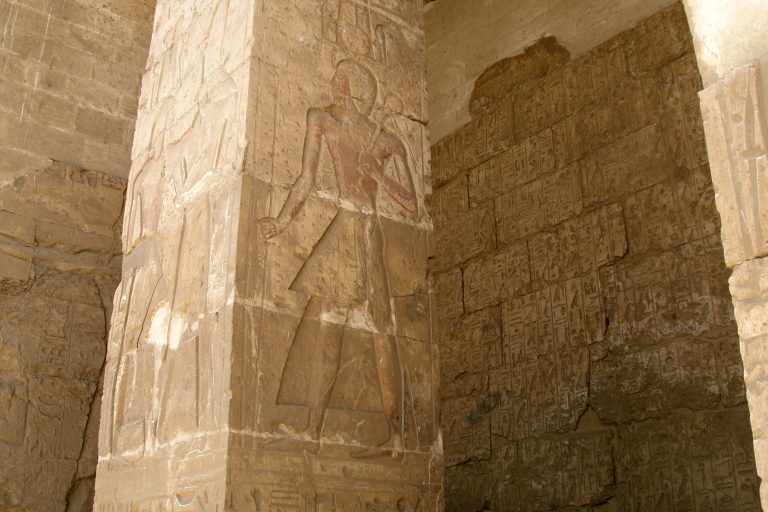 Carved standing figure beside hieroglyphic inscriptions inside the Temple of Seti I at Abydos.